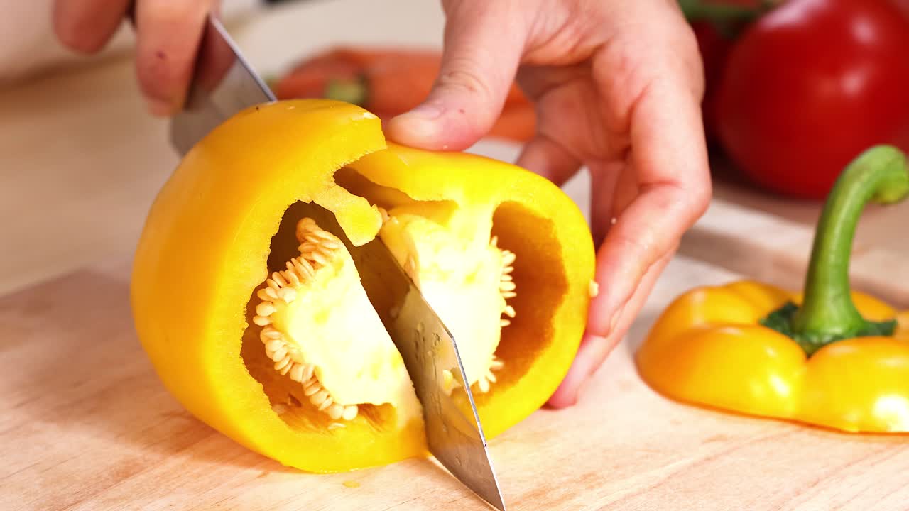 manos cortando pimientos amarillos en una tabla de madera