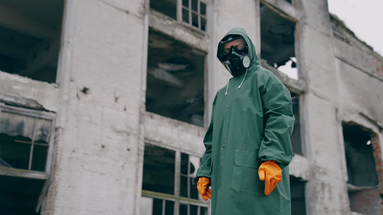 Man in protective clothing and a gas mask is standing on the background of ruined building. The concept of a post-apocalyptic world.