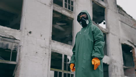 man in protective clothing and a gas mask is standing on the background of ruined building. the concept of a post-apocalyptic world.
