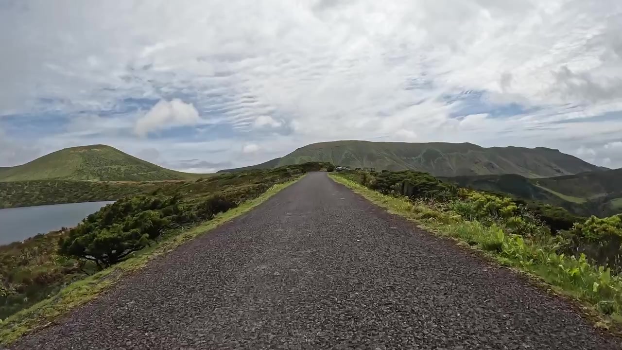 Carretera rural vacía que atraviesa colinas verdes con un lago y montañas en las Azores.