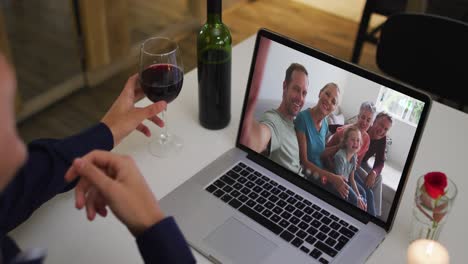 mixed race man sitting at table using laptop making video call with family