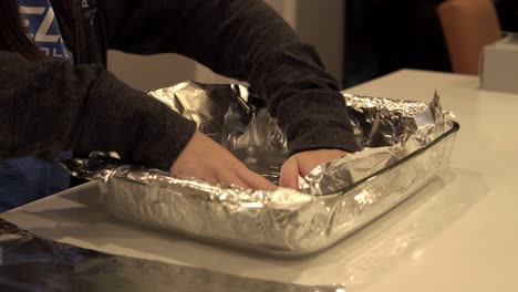 a girl lays out aluminum foil on a baking tray as prep for baking some cookies