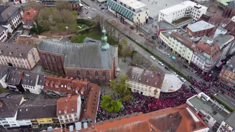 Aerial-view,-sliding-sideway-by-Altstadt-Main-street-in-Kaiserslautern-Germany-on-a-Saturday-while-FCK-Football-Club-Fans-celebrating-ther-victory-cheering,-drinking-beer-at-street-intersection