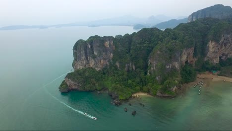 toma aérea estelar sobre acantilados de piedra caliza en una isla tropical montañosa mientras las lanchas rápidas se deslizan por las aguas debajo