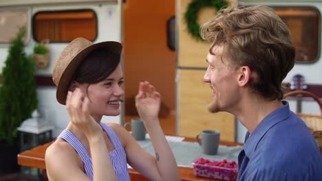 cute couple man and woman having fun together at wooden table outdoors, girl putting her hat on a man's head