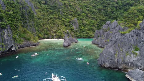 tourists kayaking and swimming in tropical emerald cadlao lagoon, tour boats anchored in the turquoise water surrounded by karst rock formations, philippines, drone shot