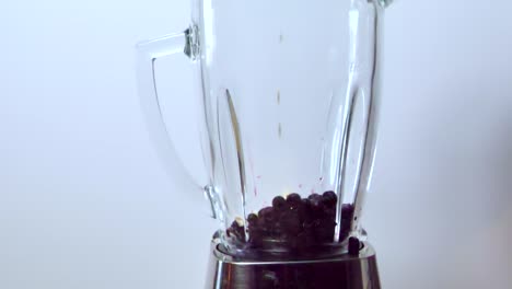 verter yogur sobre bayas azules en una licuadora, mientras se hace un batido - fondo gris - vista estática