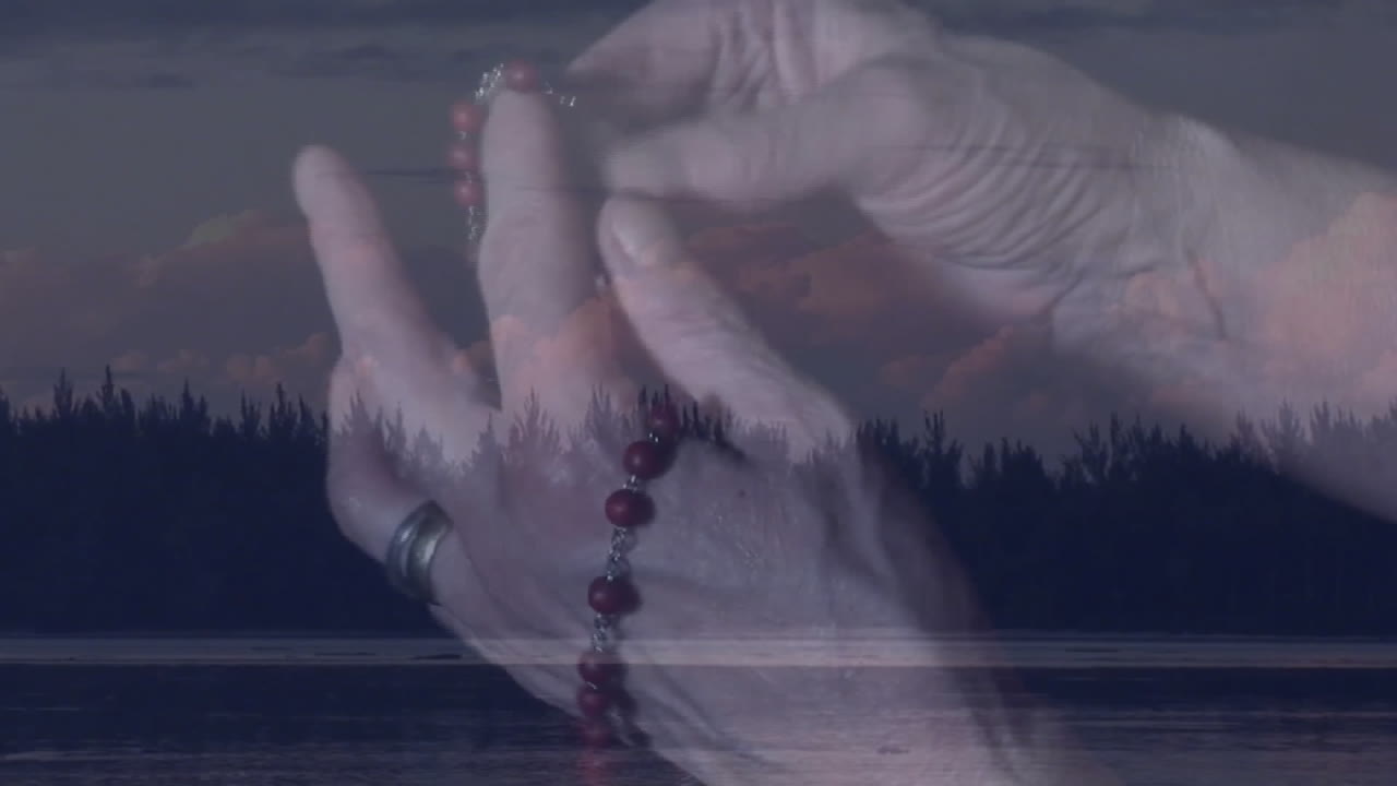 Holding prayer beads, hands over serene lake with forest in background animation