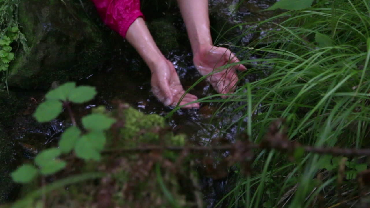 Woman drinking water on her own hands in a mystic hidden pond in Atami, Japan. Close up.