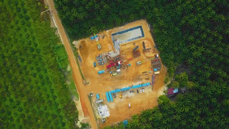 Cinematic-Drone-Shot-of-Onshore-Drilling-and-Workover-Rig-structure-and-Rig-equipment-for-oil-exploration-and-exploitation-in-the-middle-of-jungle-surrounded-by-palm-oil-trees-during-sunset-time