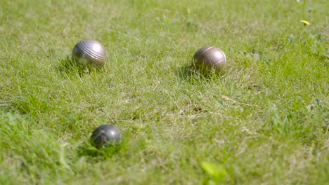 close-up view of three metal petanque balls on the grass, then the player throw another ball nearby