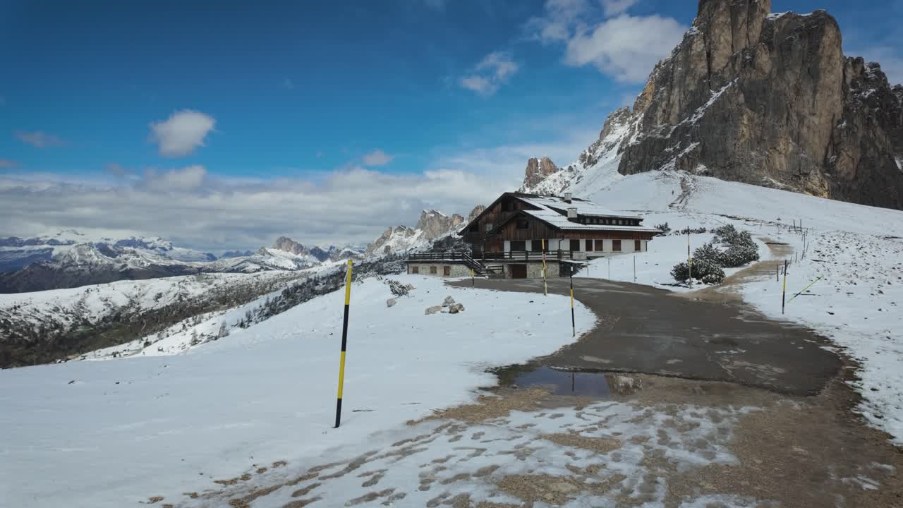 Scenic slow-motion footage of a snowy path at Passo Giau, with an alpine cabin and towering Dolomite peaks in the background