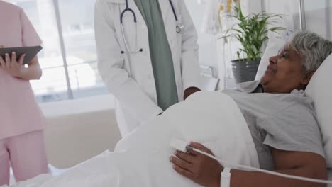 Happy-diverse-female-doctor,-nurse-with-tablet-and-senior-patient-talking-at-her-bed,-slow-motion