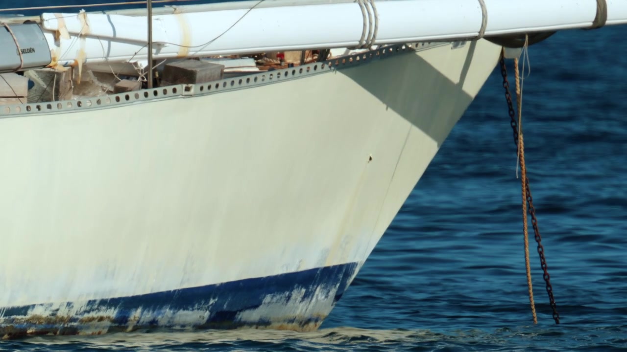 Romp van een zeilboot met ankerketting die in helder blauw water hangt, wat maritiem reizen, vrije tijd en het mariene milieu vertegenwoordigt.
