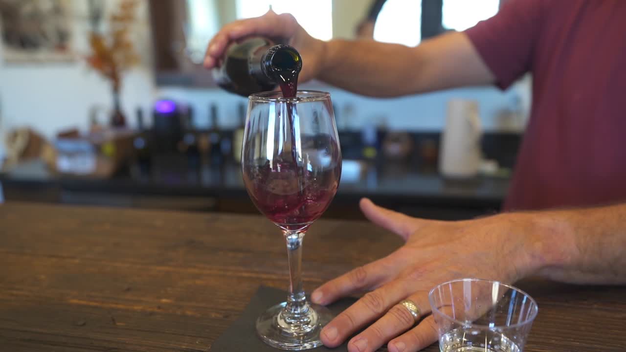 Uomo che versa vino rosso in un bicchiere durante una degustazione di vini.