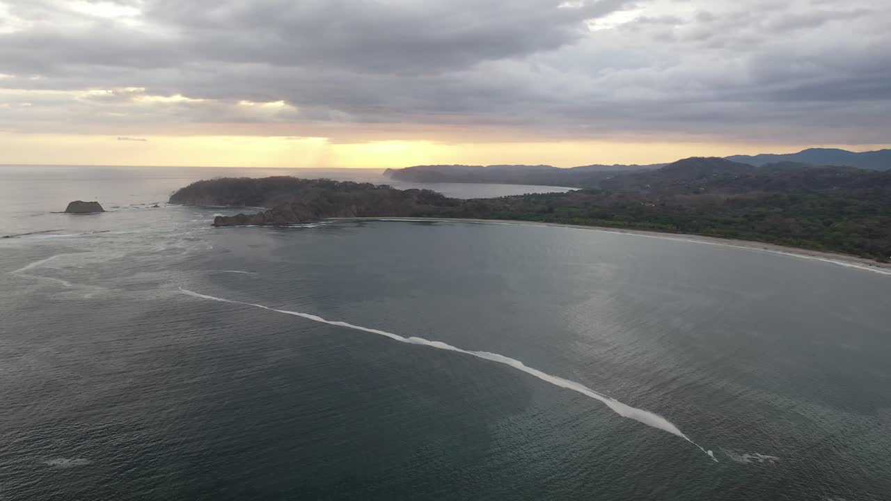 Litorale della Costa Rica dall'Oceano Pacifico al tramonto con penisola rocciosa e barriera corallina poco profonda, ripresa aerea in sorvolo.