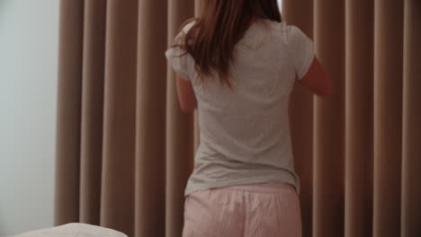 Woman-Standing-By-Bedroom-Window-In-Morning-And-Stretching