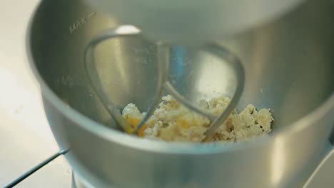 cook prepares the dough adds eggs to it mixes it in an electric mixer