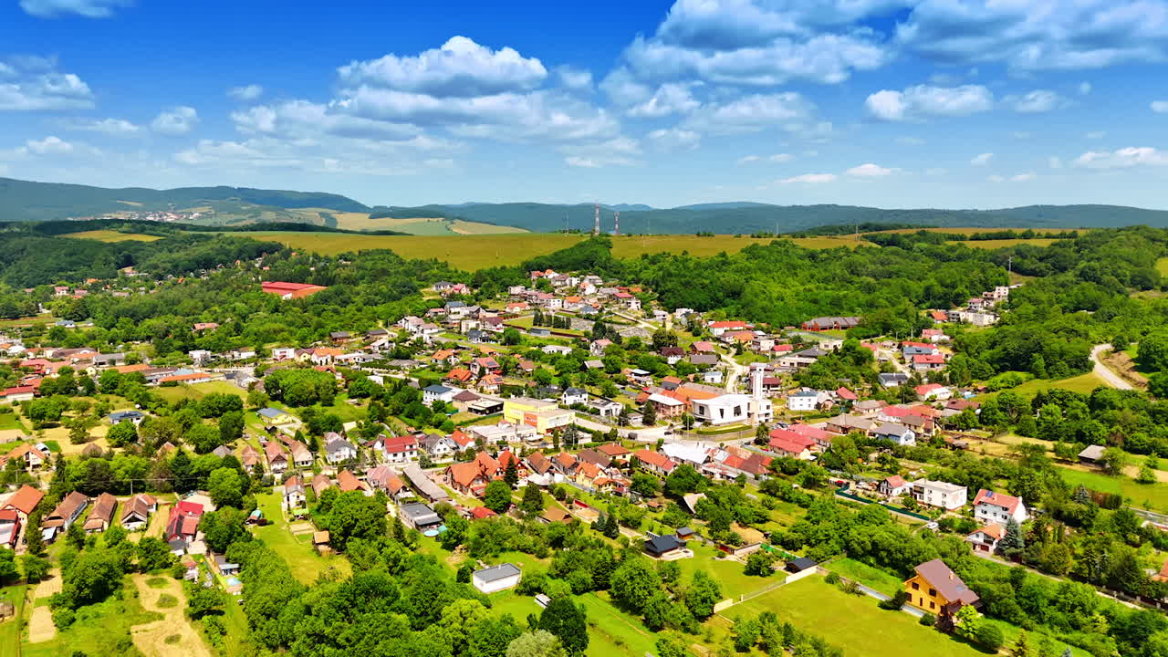 Picturesque village with greenery. Aerial view of a vibrant village surrounded by lush green hills and clear blue sky during a sunny day in spring