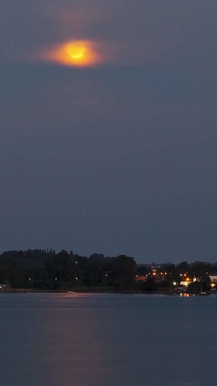 Pengambilan Gambar Panning Teluk Corfu Saat Senja: Perahu Berlabuh, Pantulan Bulan, dan Lampu Kota di Kejauhan