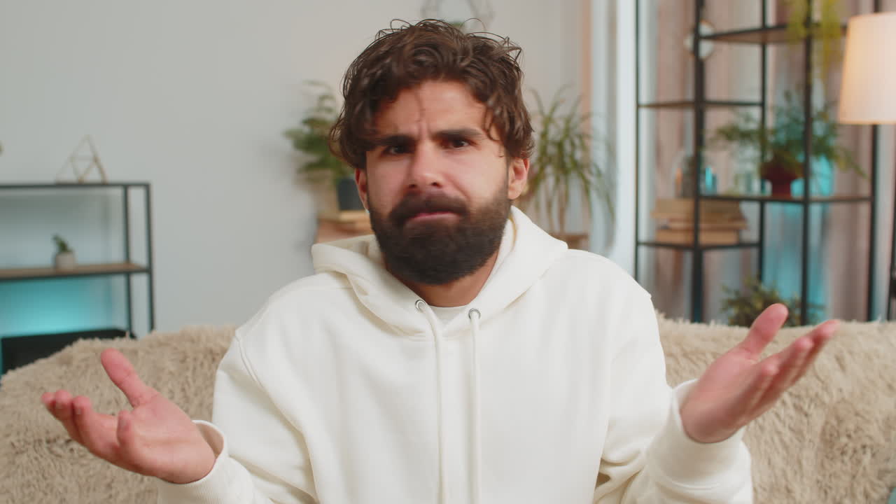 Portrait of upset indian young man making face disappointed in result bad news sitting on sofa
