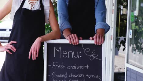 waiter and waitress standing with menu board outside the cafã©