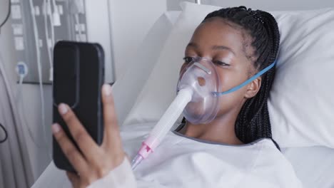 african american female patient with oxygen mask and smartphone in hospital room, slow motion