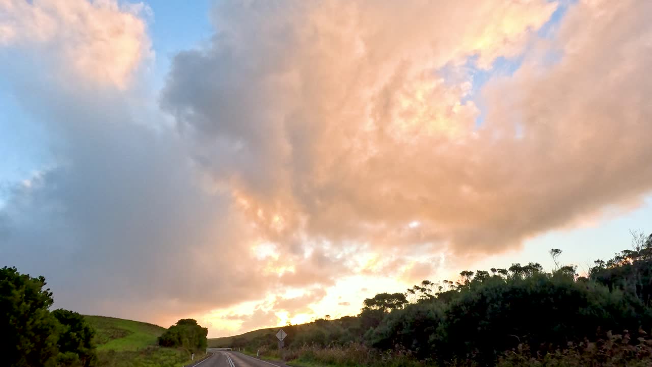A serene sunset unfolds over the Great Ocean Road, capturing vibrant clouds and lush landscapes in a tranquil setting