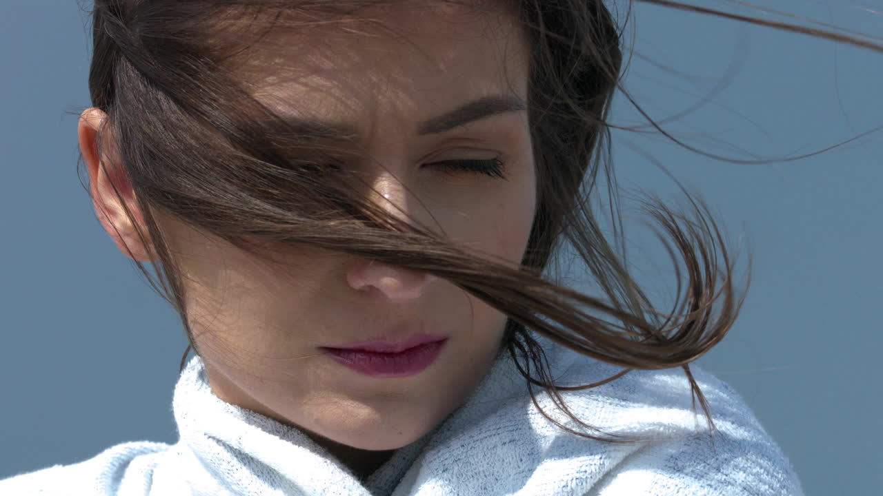 맑고 푸른 하늘을 배경으로 바람이 부는 날씨에 수건으로 싸인 사려 깊은 소녀의 초상화