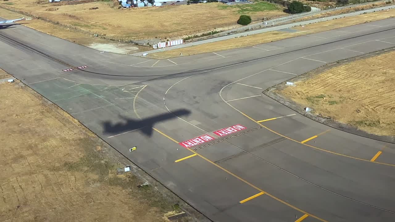 A left side aerial view taken from cockpit of the shadow of a jet airplane on short final before touchdown, flying over golden grass and the runway. daylight. 4K