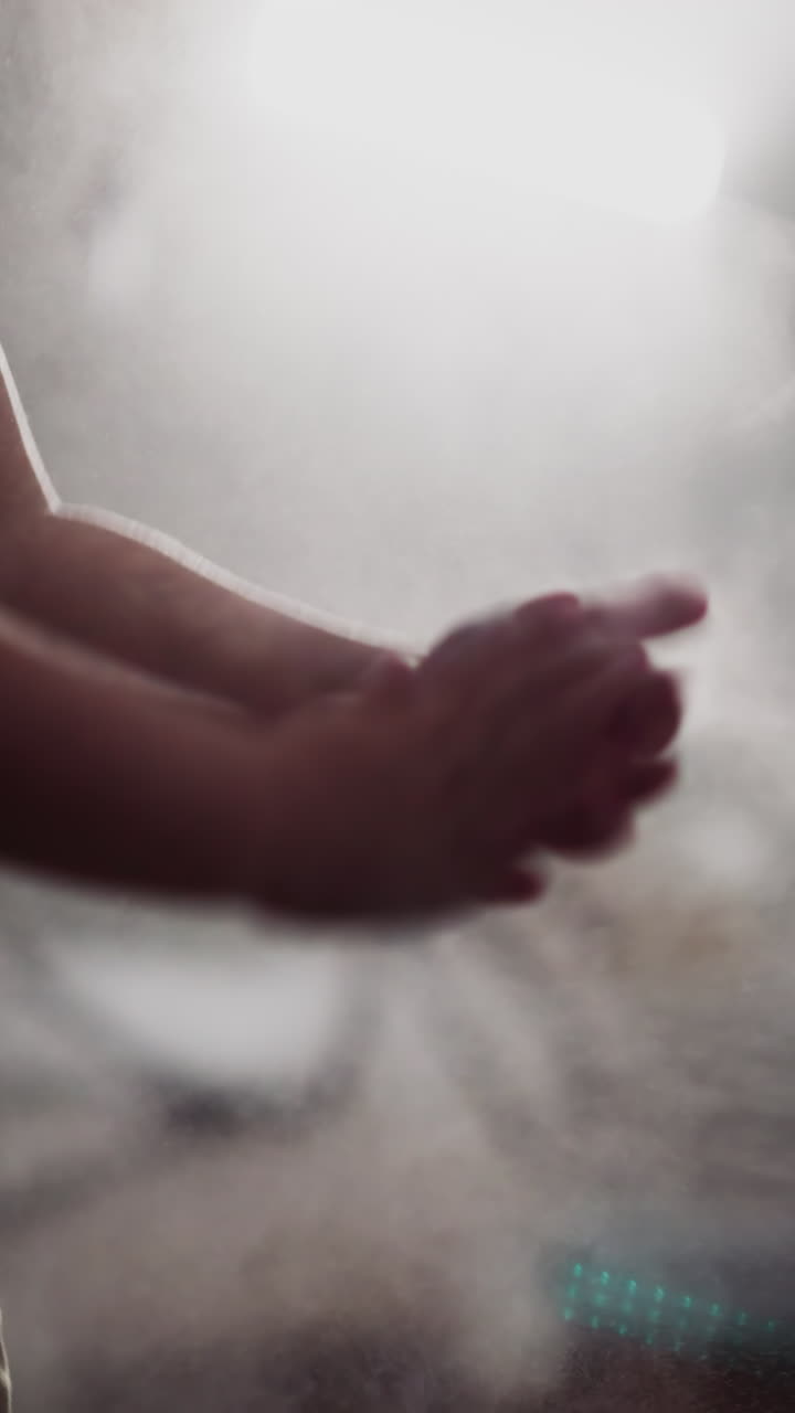 Little boy shakes off talcum powder from hands after punching bag against bright lamp illuminating room. Toddler finishes boxing class in gym closeup slow motion