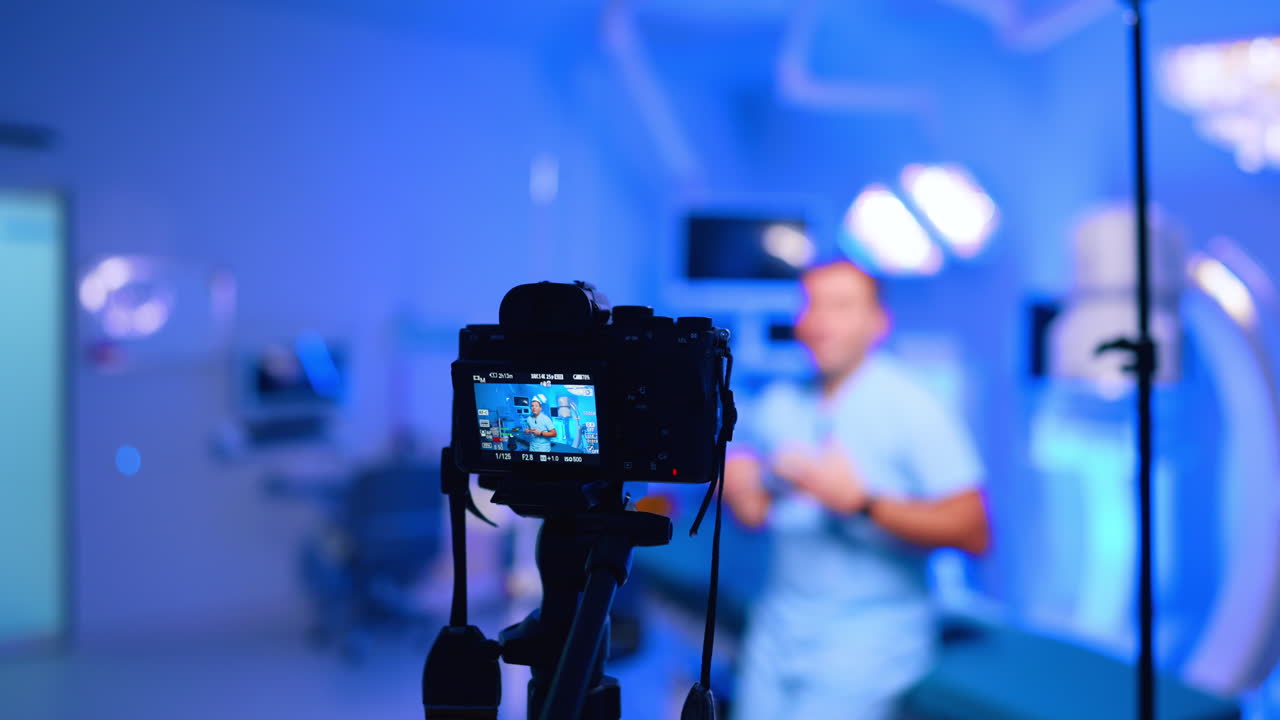 Lo schermo della fotocamera mostra un medico che registra un vlog in clinica. Lo schermo della fotocamera mostra il medico in camice, con uno sfondo clinico sfocato, illuminazione blu e una profondità di campo ridotta.