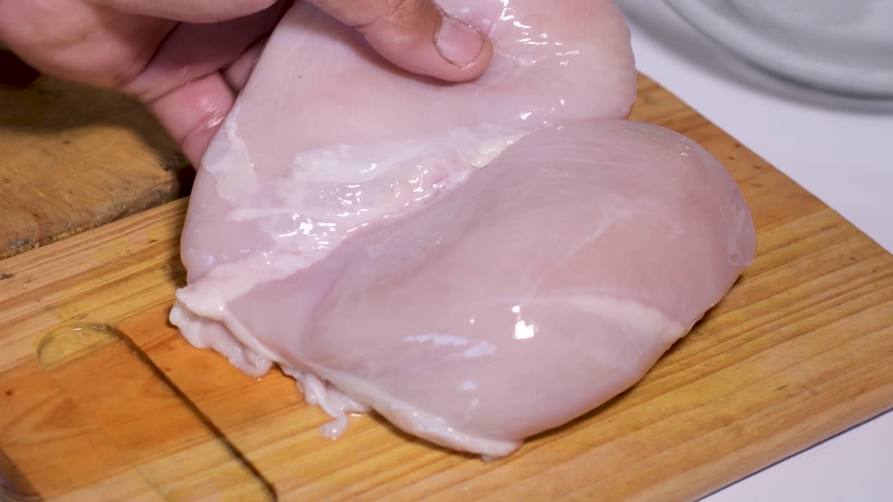 las manos cortan la pechuga de pollo cruda en tiras en una tabla de cortar de madera