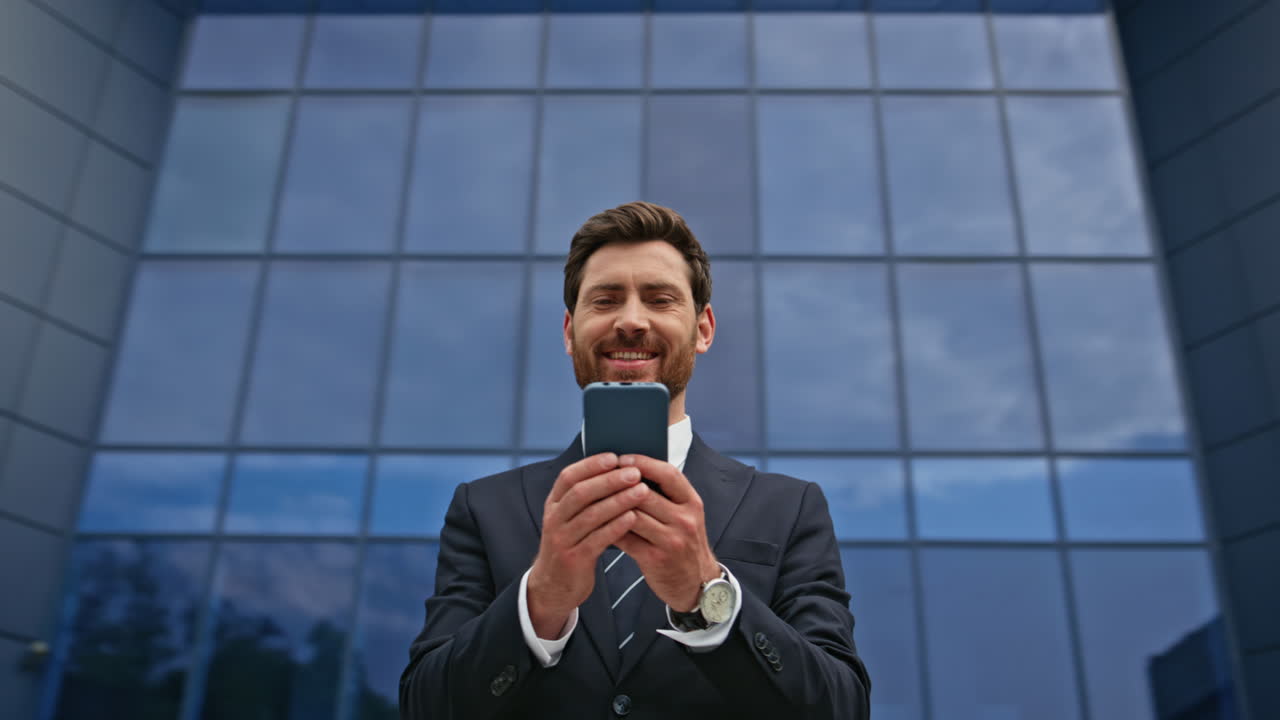 Smiling executive looking smartphone standing in front glass building closeup