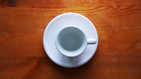 top shot of an ampty espresso cup standing on a white plate on a brown wooden table