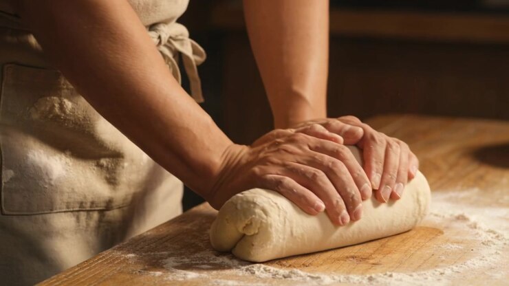 Starting pressing palms, hands rolling dough and forming loaf on floured kitchen counter in apron