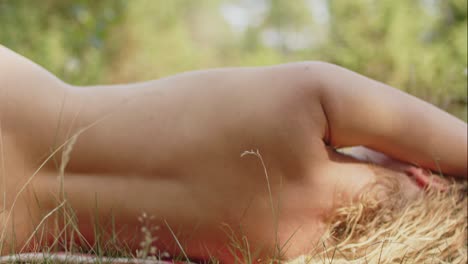 a woman lying on her side with the back towards the camera in a green forest on a sunny summer day