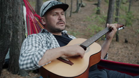 man playing guitar in a hammock in a forest