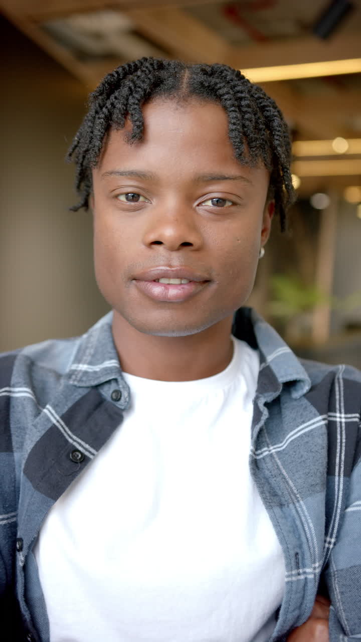 Vertical video: Smiling man in casual shirt looking at camera in modern office setting