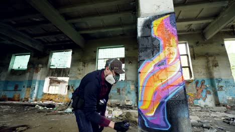 urban street artist is painting graffiti in abandoned building with dirty walls and windows, he is using paint spray. modern artwork and creative people concept.