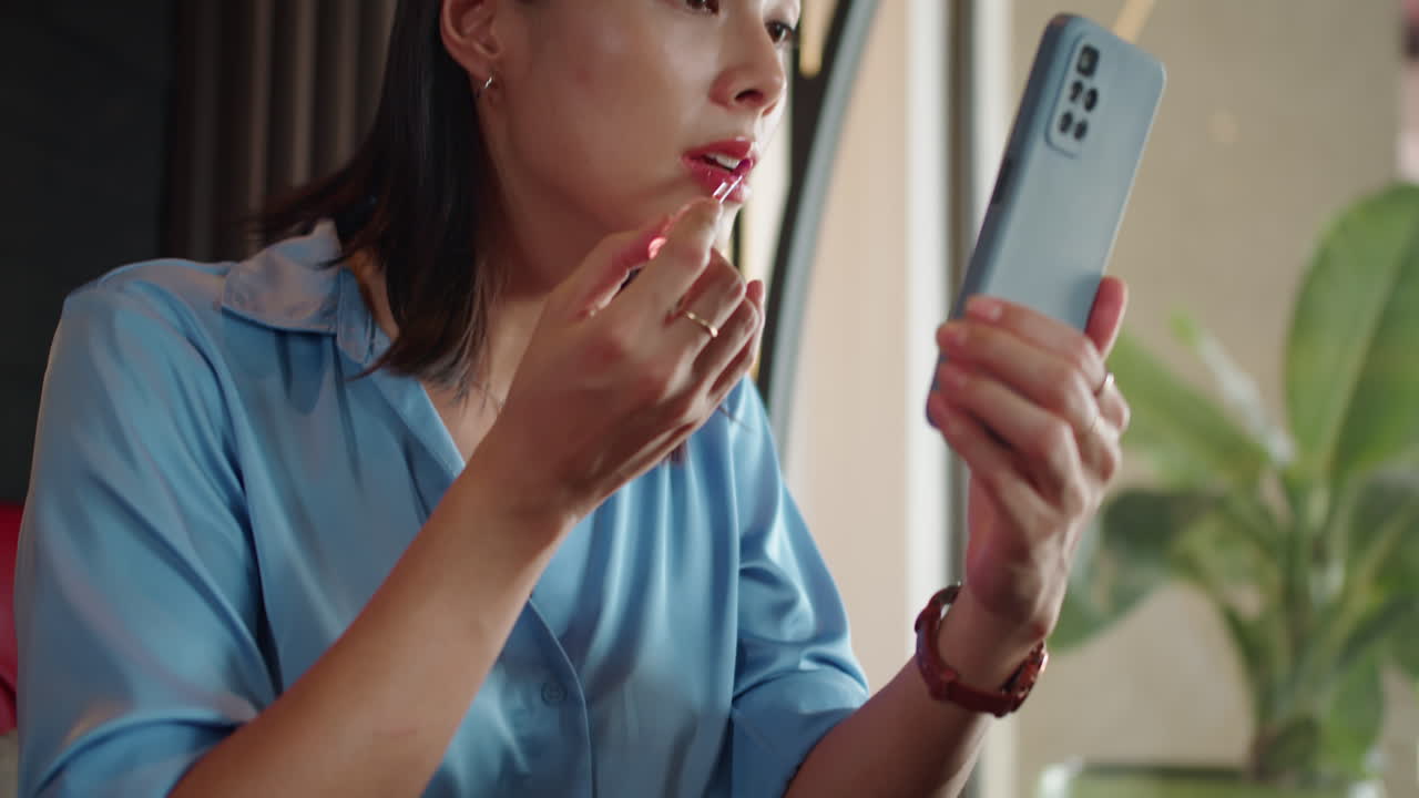 Asian Employee Applying Gloss on Lips in front of Smartphone