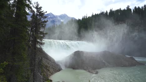 revealed amongst the evergreens is a large waterfall, creating mist as it hits the mountainous rocks below