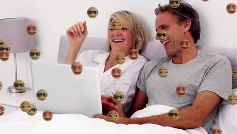 animation of face emoji icons against caucasian senior couple having a videocall on laptop in bed