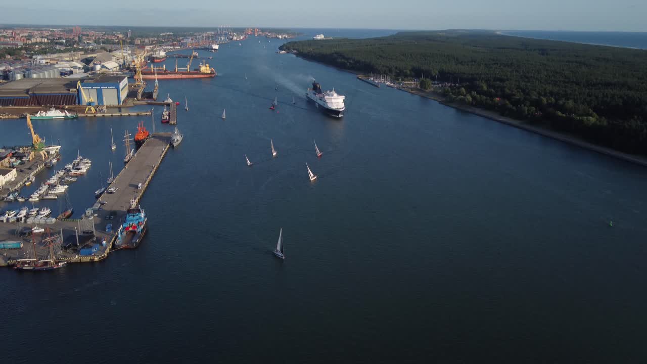 Små segelbåtar och massiv färja lämnar Klaipedas hamn.