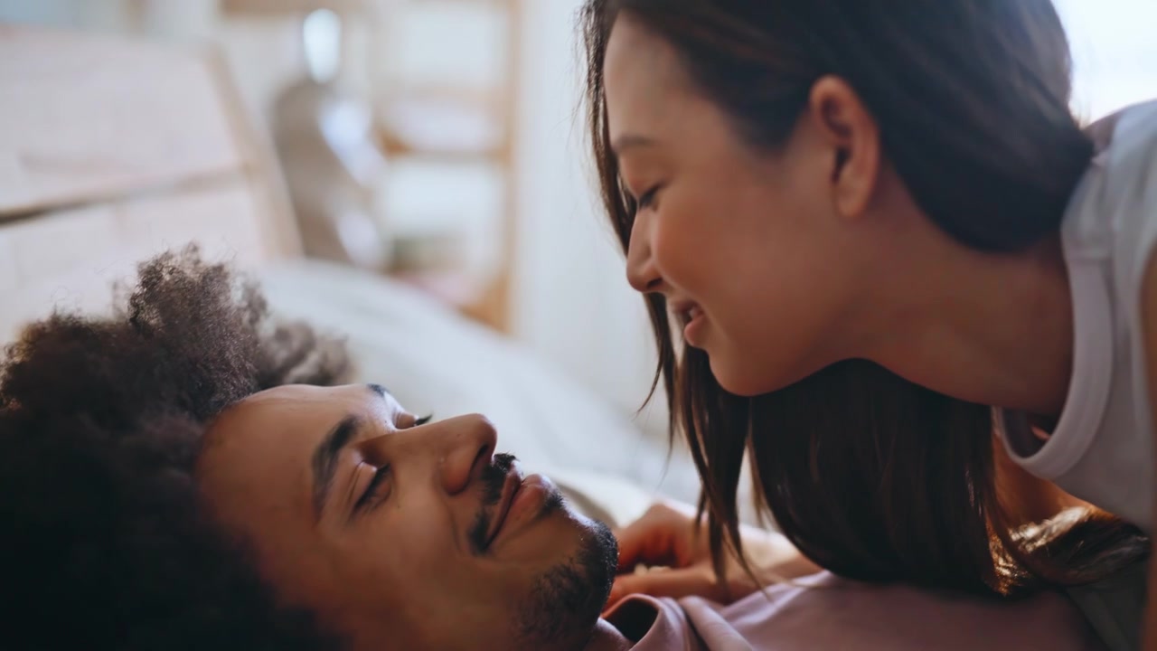 Woman kissing sleeping man in bed. Close up girlfriend touching nose morning.