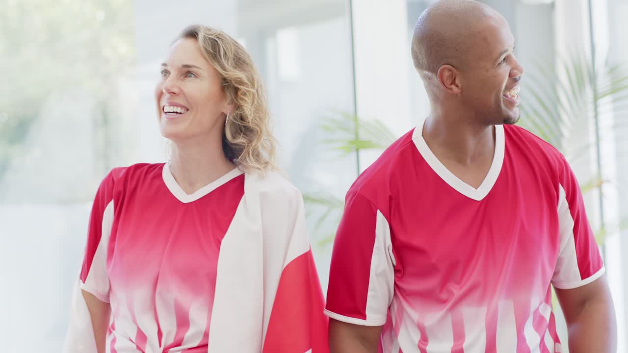 Equipo diverso con camisetas rojas, hombre afroamericano aplaudiendo, estrechando manos junto a ventanas reaccionando fuera de pantalla