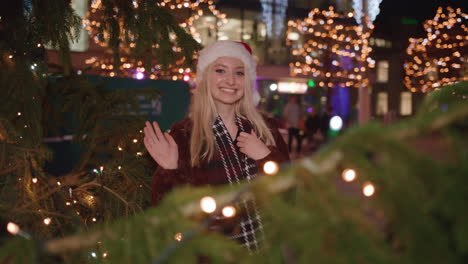 mujer joven sorprende a su pareja saliendo de detrás del árbol de navidad y sonriendo