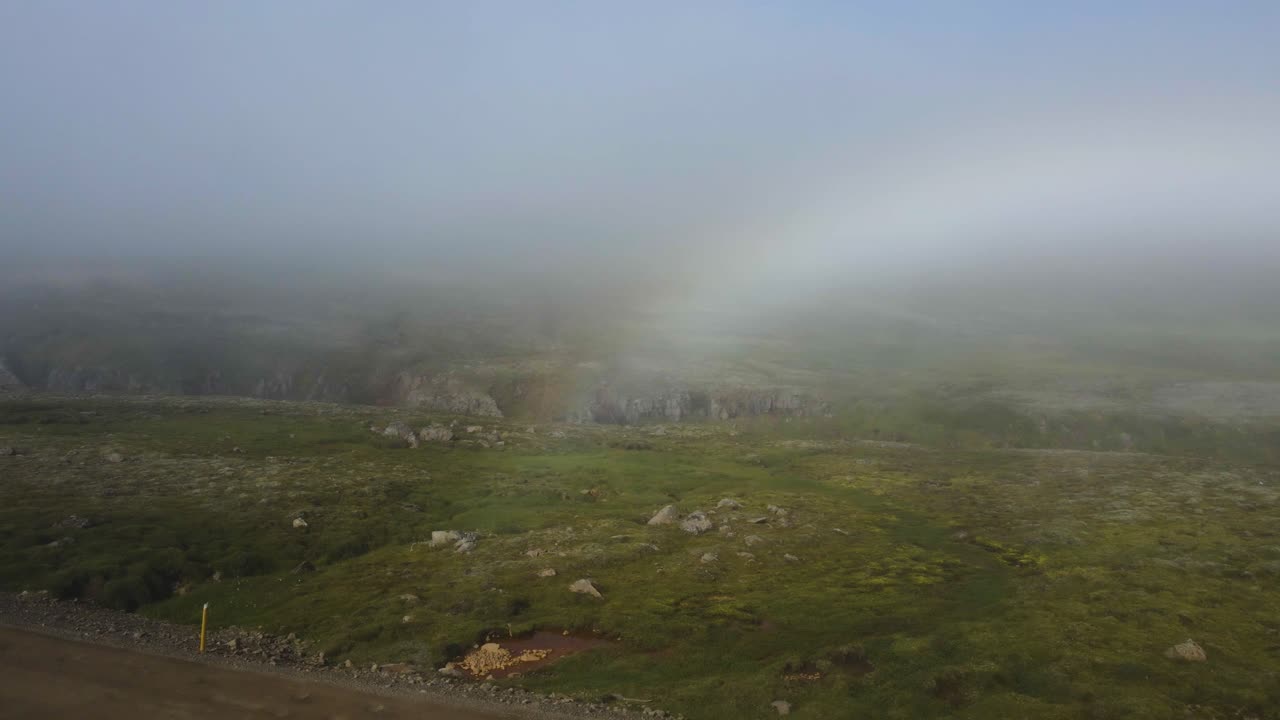 Unveil a surprise rainbow emerging through the fog atop an Icelandic mountain, post-rainstorm &mdash; a mystical moment in crisp 4K, captured by drone
