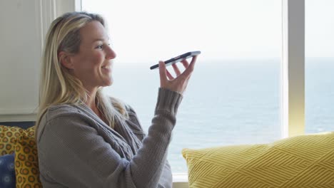 happy caucasian mature woman looking through the window and using smartphone