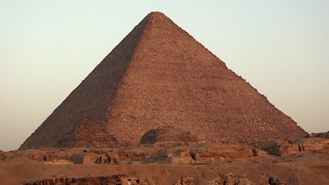 Camels walk past base of Khufu pyramid in golden Giza desert of Egypt